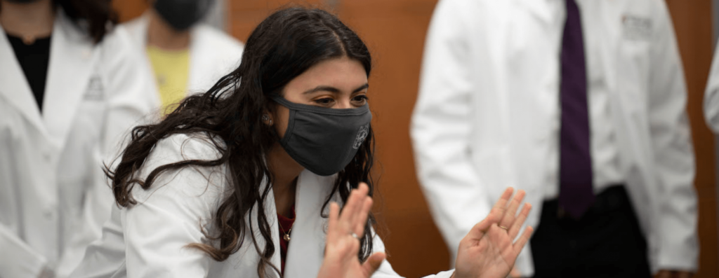 First-year medical student Sneha Chaturvedi waves at her friends and family watching at home after they took part in a “White Coat Reflection.” Because of restrictions due to covid-19 coronavirus, they received their white coats and started their medical journey with a small group of students, their coach, and family and friends watching remotely on September 11, 2020. MATT MILLER/WASHINGTON UNIVERSITY SCHOOL OF MEDICINE