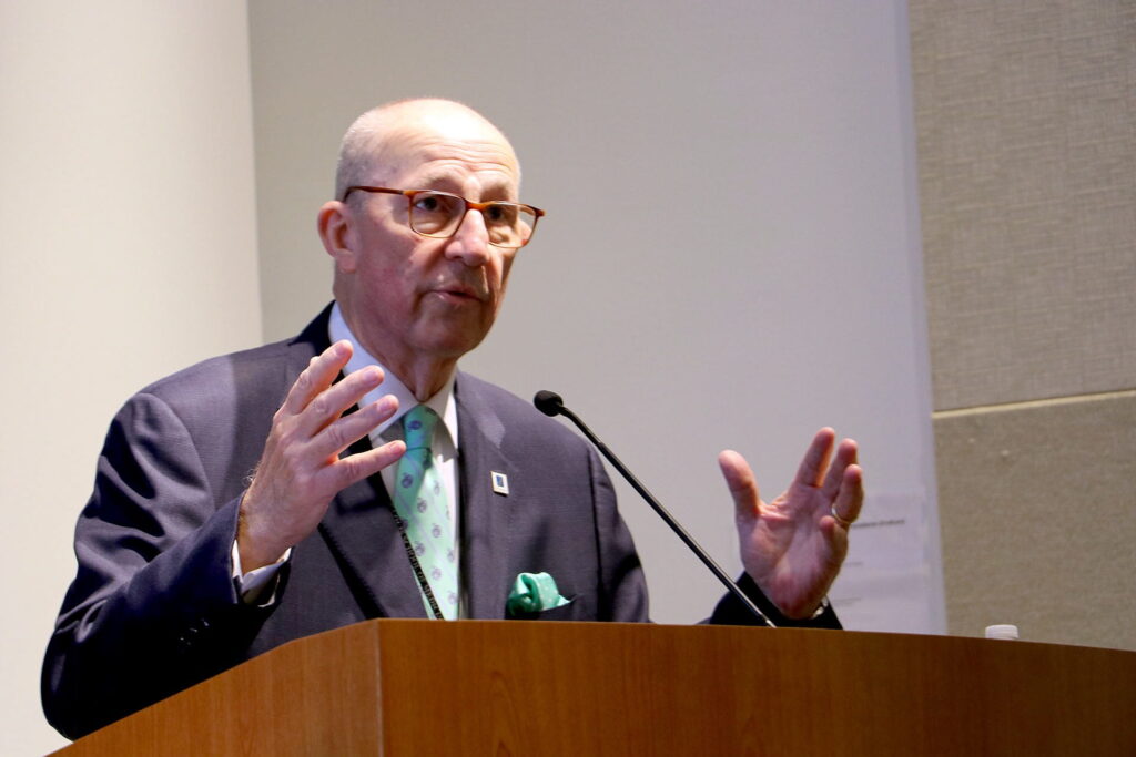 Dr. Eberlein in suit and tie at podium delivering lecture.