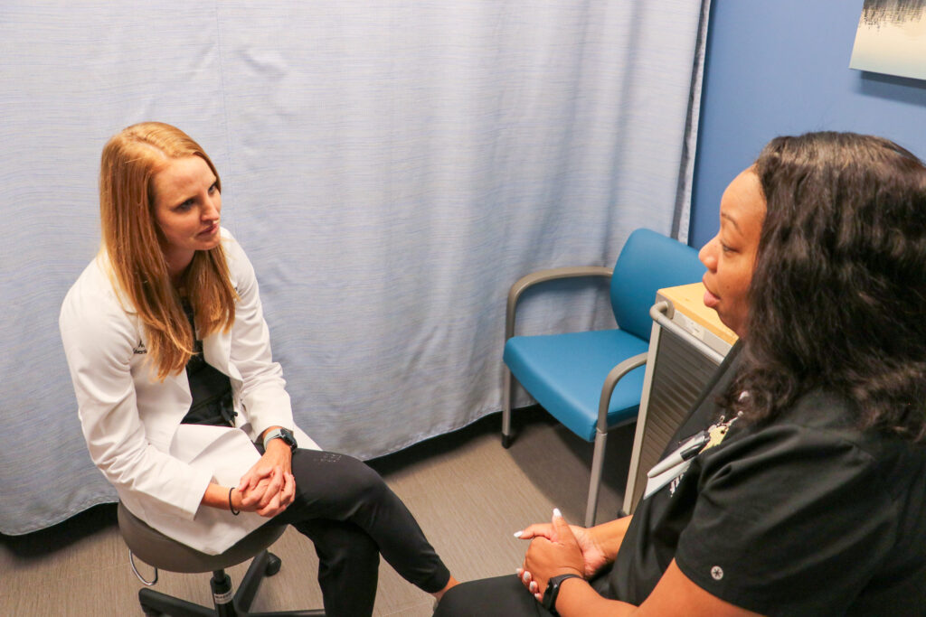 Nurse in white coat with patient in clinic room.