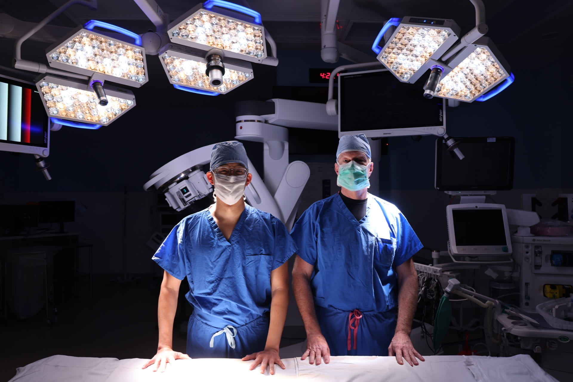 Doctors Kim and Figenshau stand in front of single port robot in an operating room.
