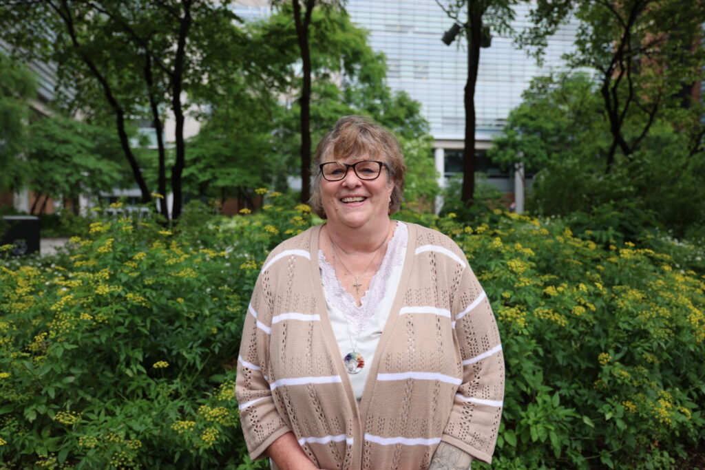 Ginny Devenport standing outside on the medical campus with flowers and trees in background.
