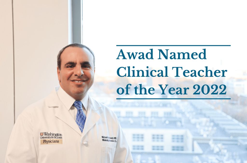 Surgeon educator Michael Awad in white coat standing in front of window on medical campus.
