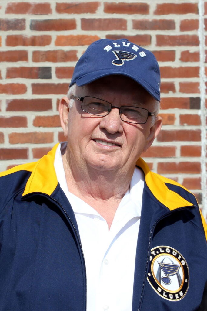 Vojin Bozovich wearing St. Louis Blues hat and jacket, standing in front of brick wall.