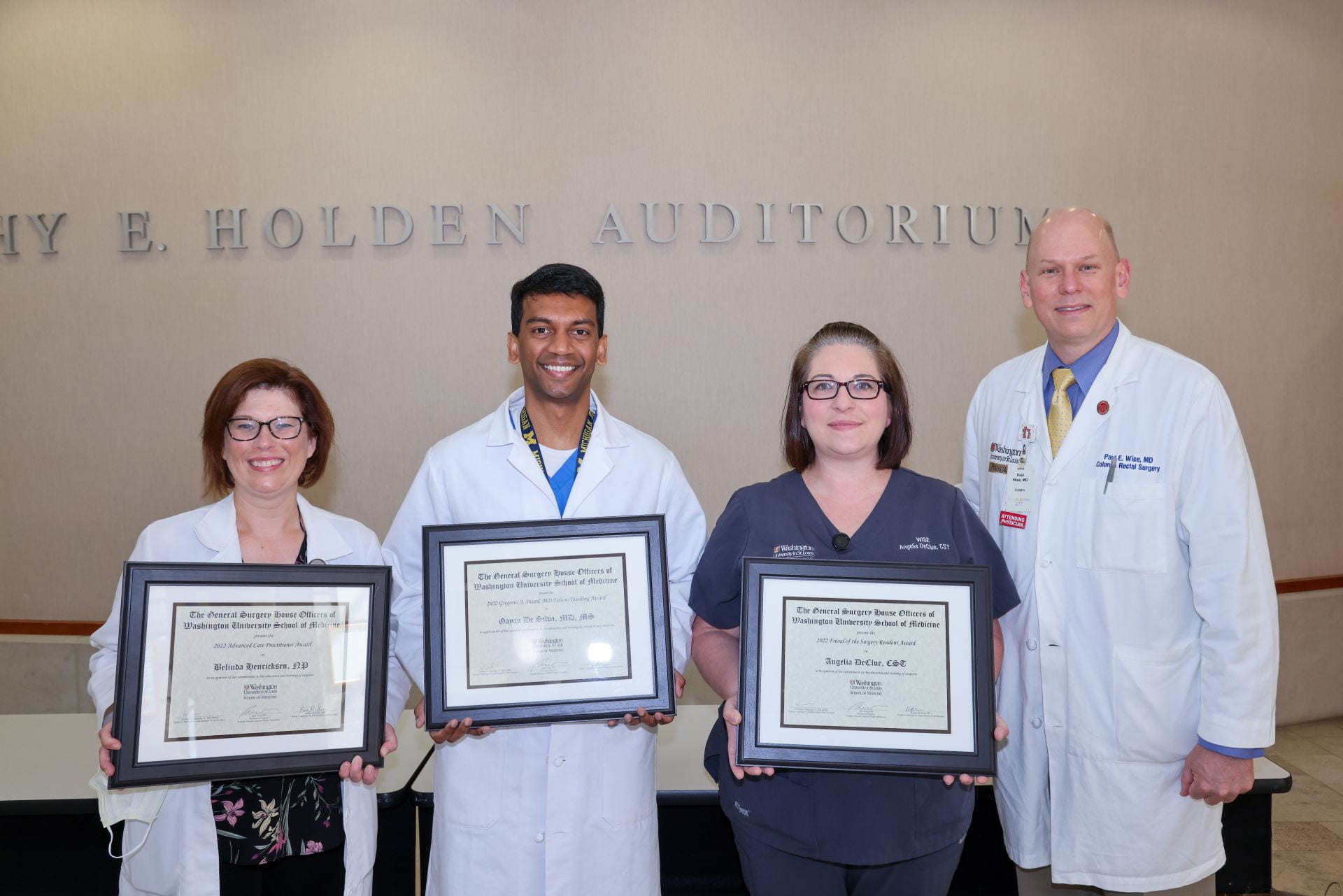 Award recipients holding framed certificates outside Holden Auditorium at school of medicine with Paul Wise in white coat.