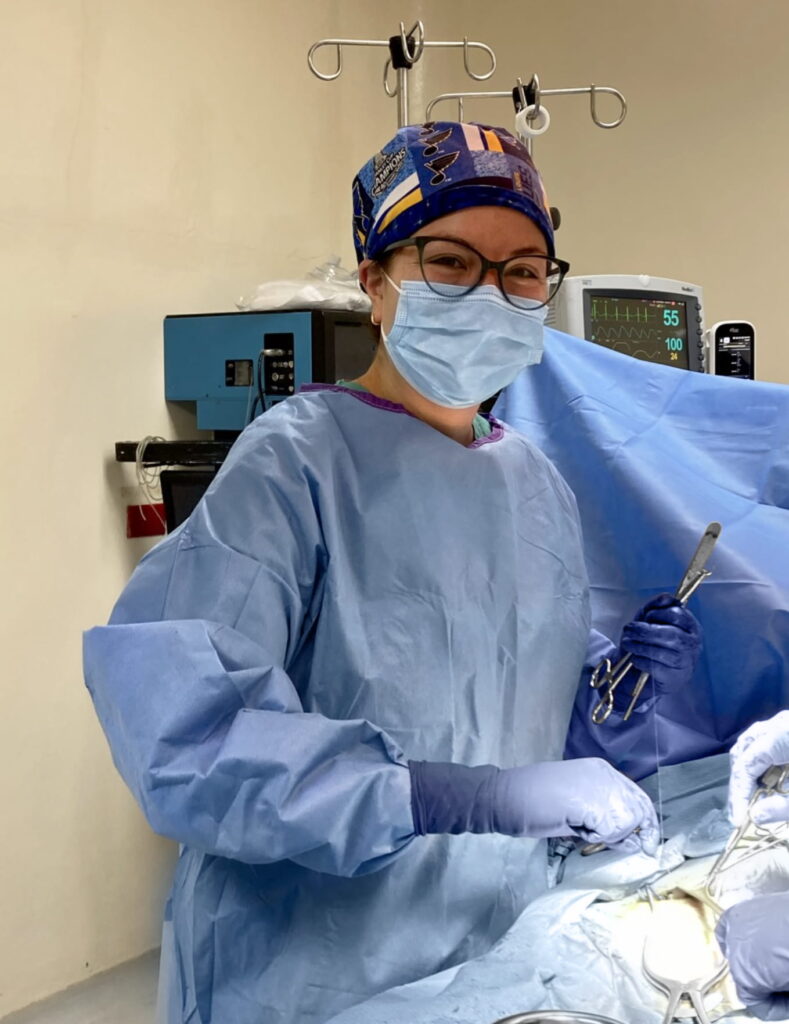 Surgeon Meghan Kelly in blue scrubs and St. Louis Blues scrub cap holding scalpel and surgical tools in operating room