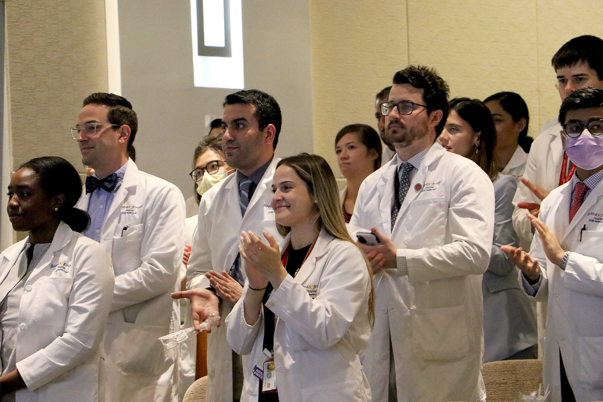 Surgery residents in white coats applauding award recipients.