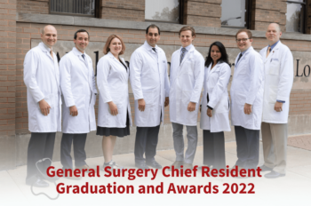 General surgery residents and faculty in white coats standing together outside medical center campus.